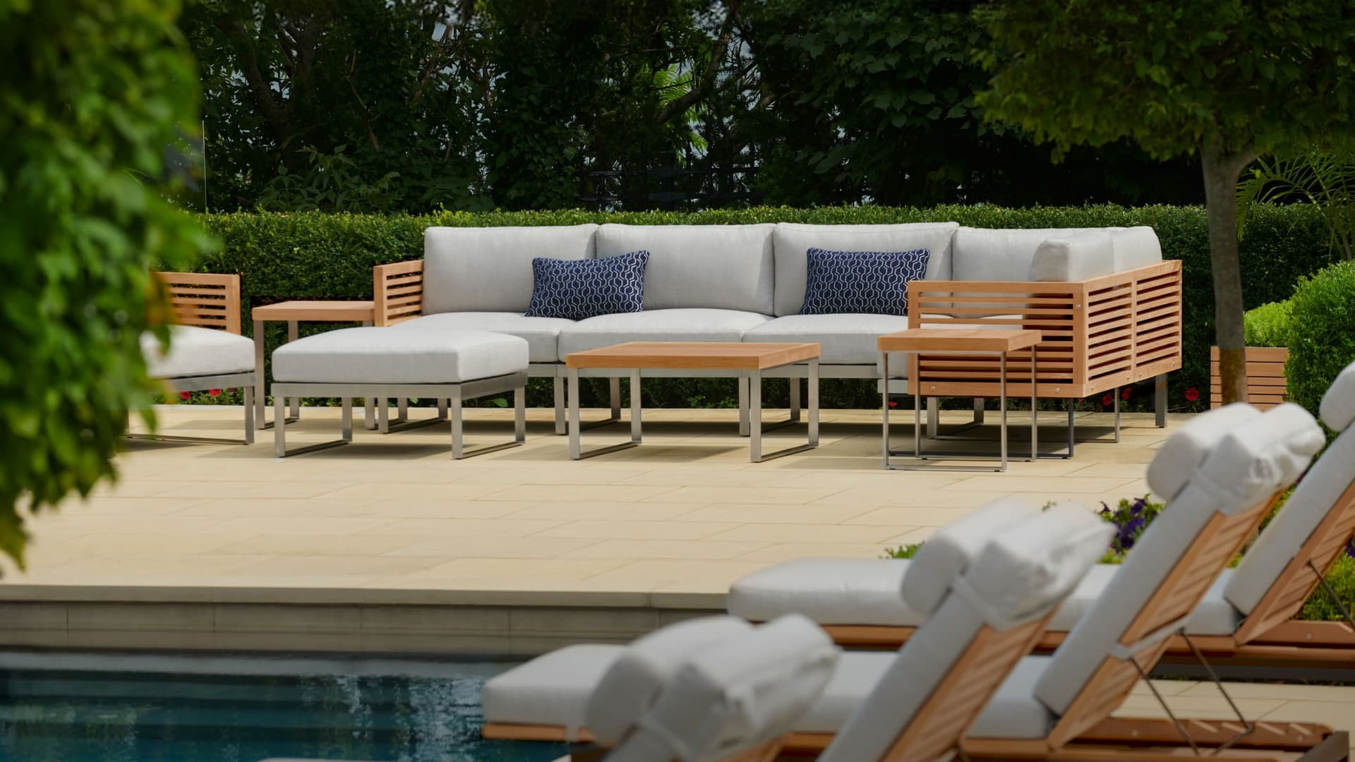 NewAge teak outdoor sectional, ottoman and coffee tables on a poolside patio