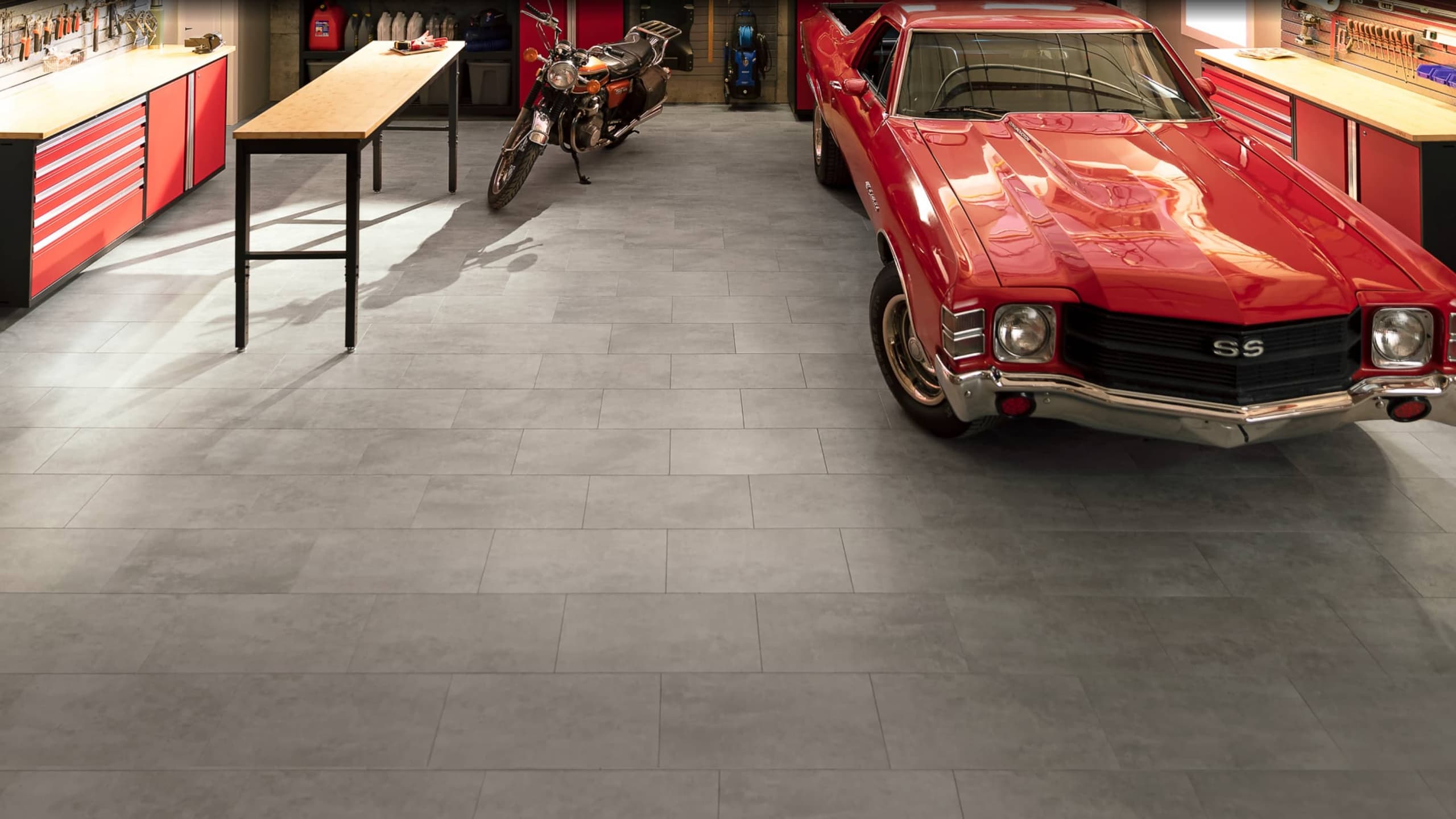 Close-up of grey NewAge garage floor tiles beneath the wheel of a red classic car